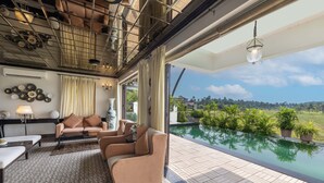 A spacious living area with a large window overlooking a swimming pool and lush greenery. - Echor Reis Magos Villa Goa (Verem)
