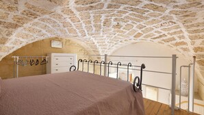 Een slaapkamer met een stenen plafond, een bed met een bruine sprei, een witte dressoir en een metalen leuning.