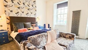 A bedroom with a large bed, a patterned headboard, a window with curtains, and a unique patterned sofa. - No 1 @ The Rocket Rooms Apartments (Berwick-upon-Tweed)