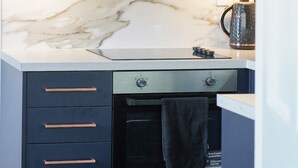 A modern kitchen with dark cabinetry, a marble backsplash, and a built-in oven. - No 1 @ The Rocket Rooms Apartments (Berwick-upon-Tweed)