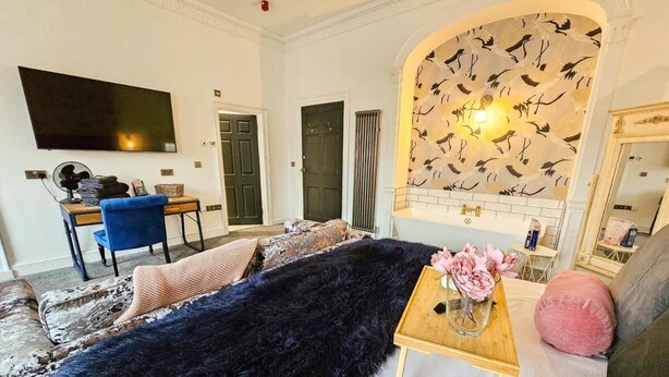 A living room with a large dark fur rug, a wooden side table with a vase of flowers, and a blue chair. - No 1 @ The Rocket Rooms Apartments (Berwick-upon-Tweed)