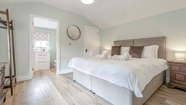 Een slaapkamer met een groot bed, een nachtkastje, een houten trap en een badkamer zichtbaar door een open deur.