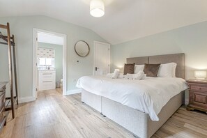 Une chambre à coucher avec un grand lit, une table de chevet, une échelle en bois et une salle de bain visible à travers une porte ouverte.