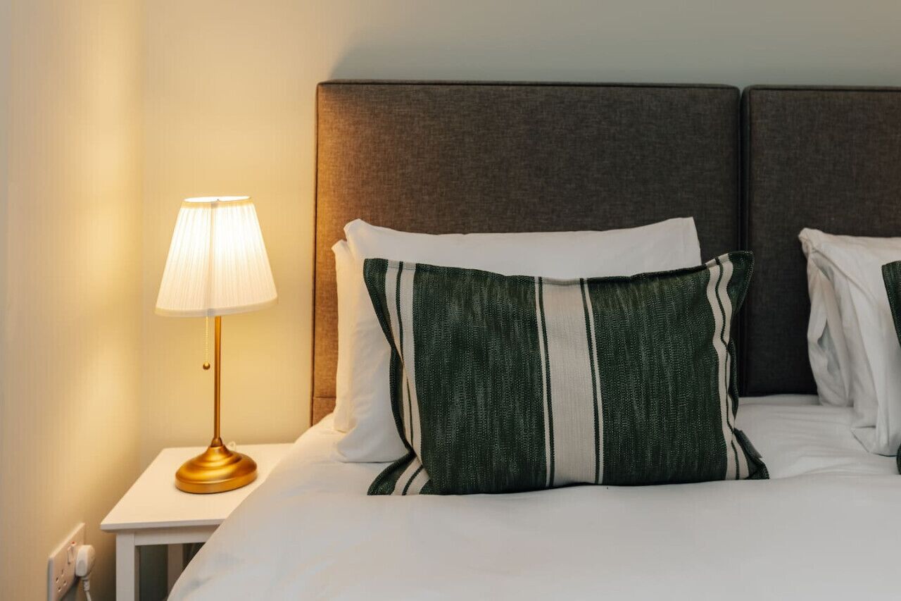 A hotel room with a bed, a nightstand, a lamp, and two pillows.