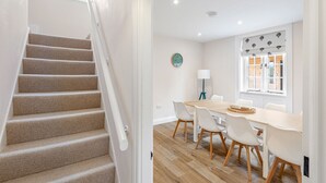 Een modern interieur met een trap, een eethoek met een houten tafel en stoelen, en een raam met uitzicht op een gebouw.