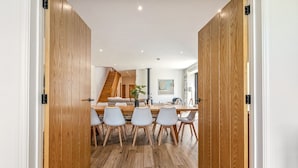 A modern dining area with a wooden floor, white chairs, and a central table. - Home farm barn - Pet friendly close to Oxford (Nuneham Courtenay)