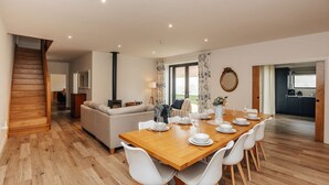 A spacious living area with a wooden staircase, a dining table set for four, and a kitchen visible through an open door. - Home farm barn - Pet friendly close to Oxford (Nuneham Courtenay)