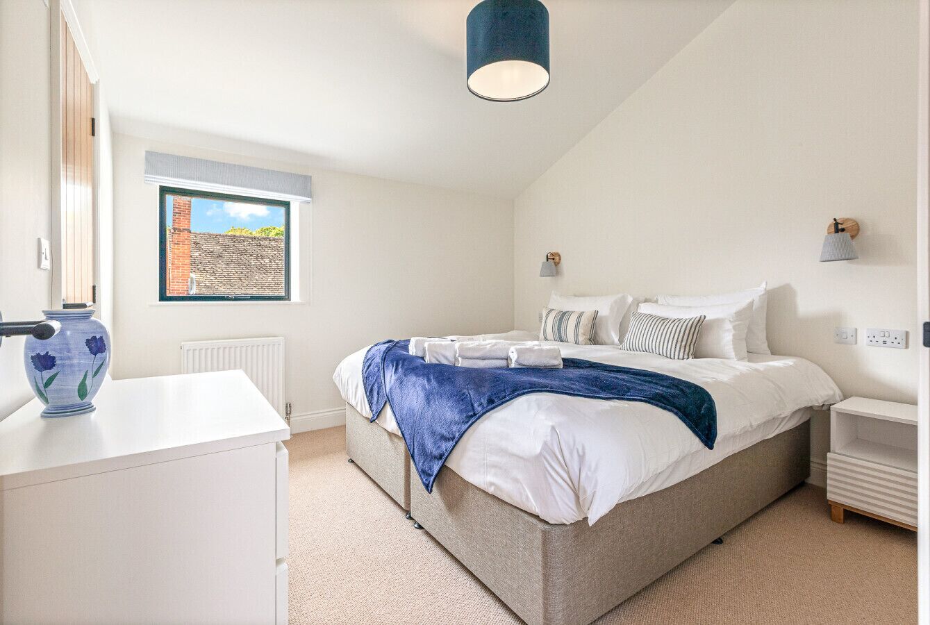 A bedroom with a bed, bedside tables, a lamp, a window, and a vase on a dresser.