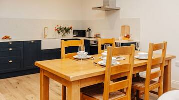 Un coin repas avec une table et des chaises en bois, un évier blanc et un four à micro-ondes à l’arrière-plan.