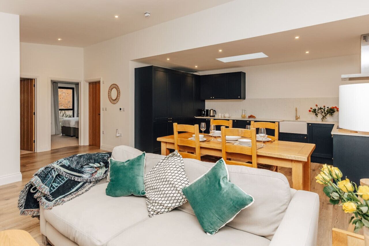 Ein modernes Wohnzimmer mit einer Couch, grünen Kissen und einem Essbereich mit einem Holztisch und Stühlen.