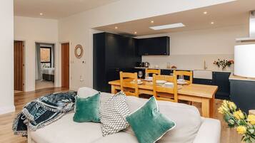 Ein modernes Wohnzimmer mit einer Couch, grünen Kissen und einem Essbereich mit einem Holztisch und Stühlen.