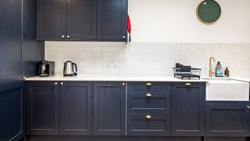 Una cocina moderna con armarios oscuros, una encimera blanca, cafetera, hervidor, pileta con grifo y un reloj de pared.