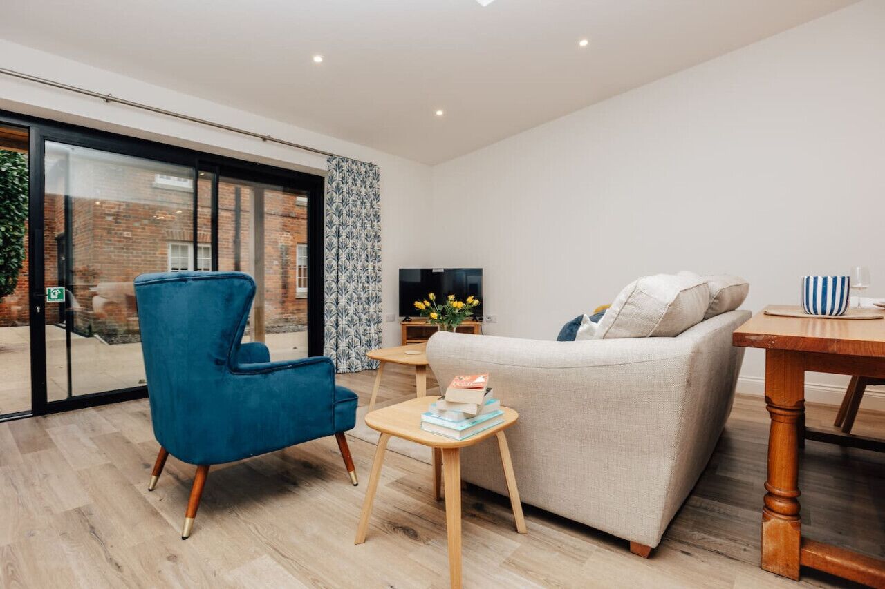 A modern living room with a blue armchair, a beige sofa, a wooden coffee table, and a TV on a stand.