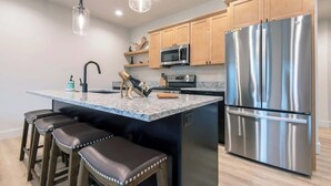 Una cucina moderna con isola centrale, elettrodomestici in acciaio inossidabile, mobili in legno e una lampada a sospensione.