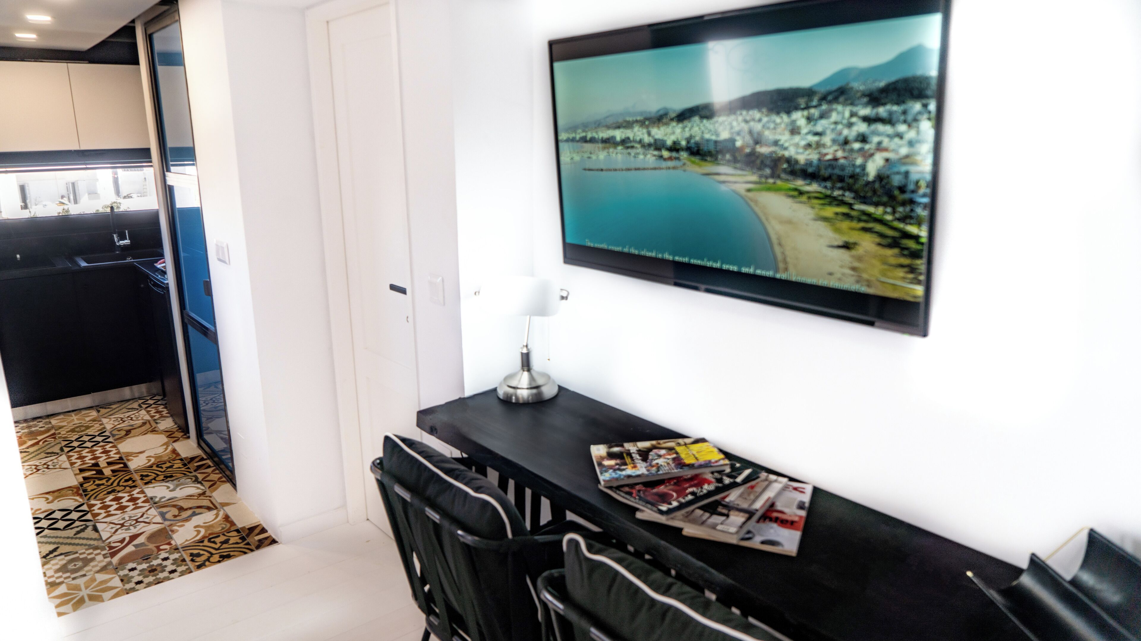 Une chambre d’hôtel dotée d’une grande télévision diffusant un paysage magnifique, d’une petite table avec un magazine et d’un tapis à motifs sur le sol.