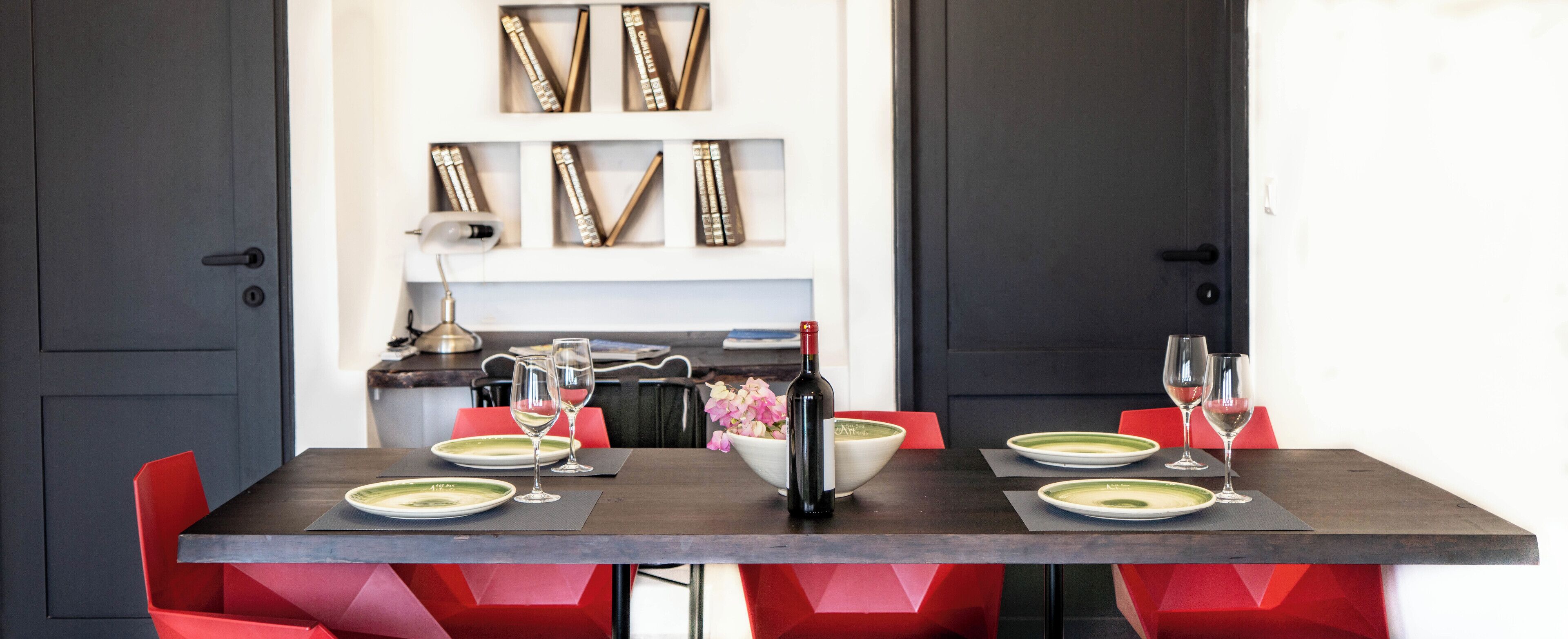 A dining table set with plates, glasses, and a bottle, surrounded by red chairs.