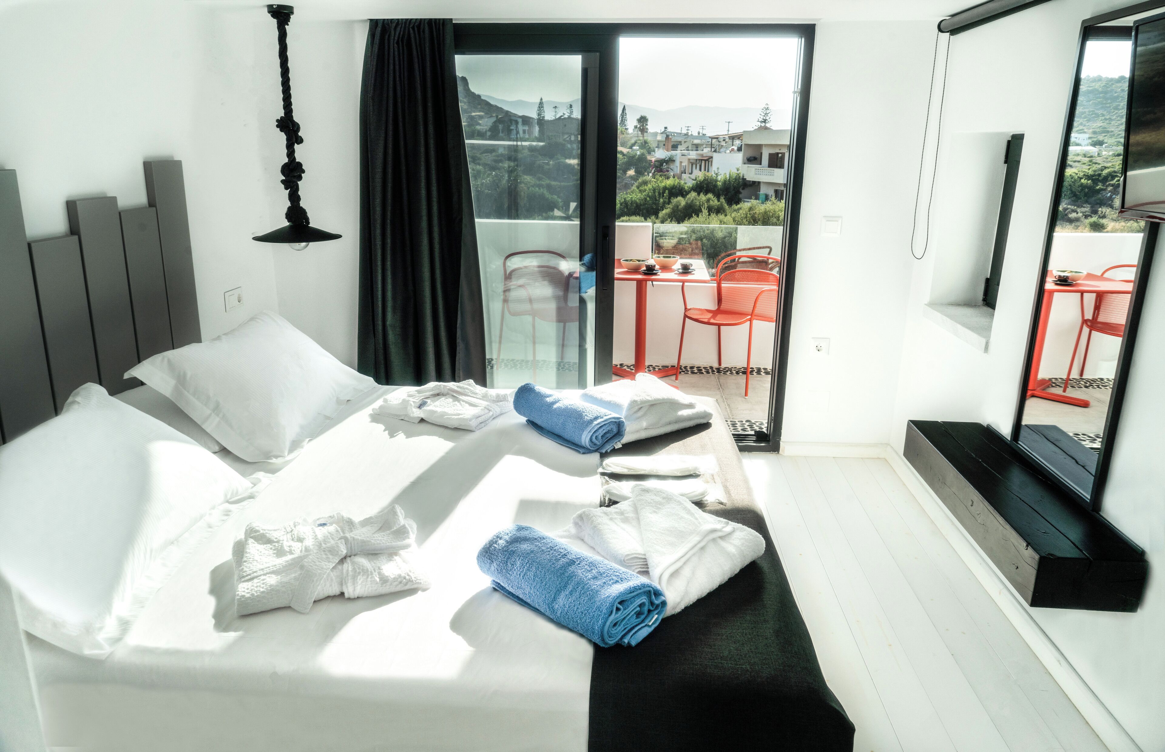 A hotel room with a bed, a balcony with red chairs, and a TV on the wall.