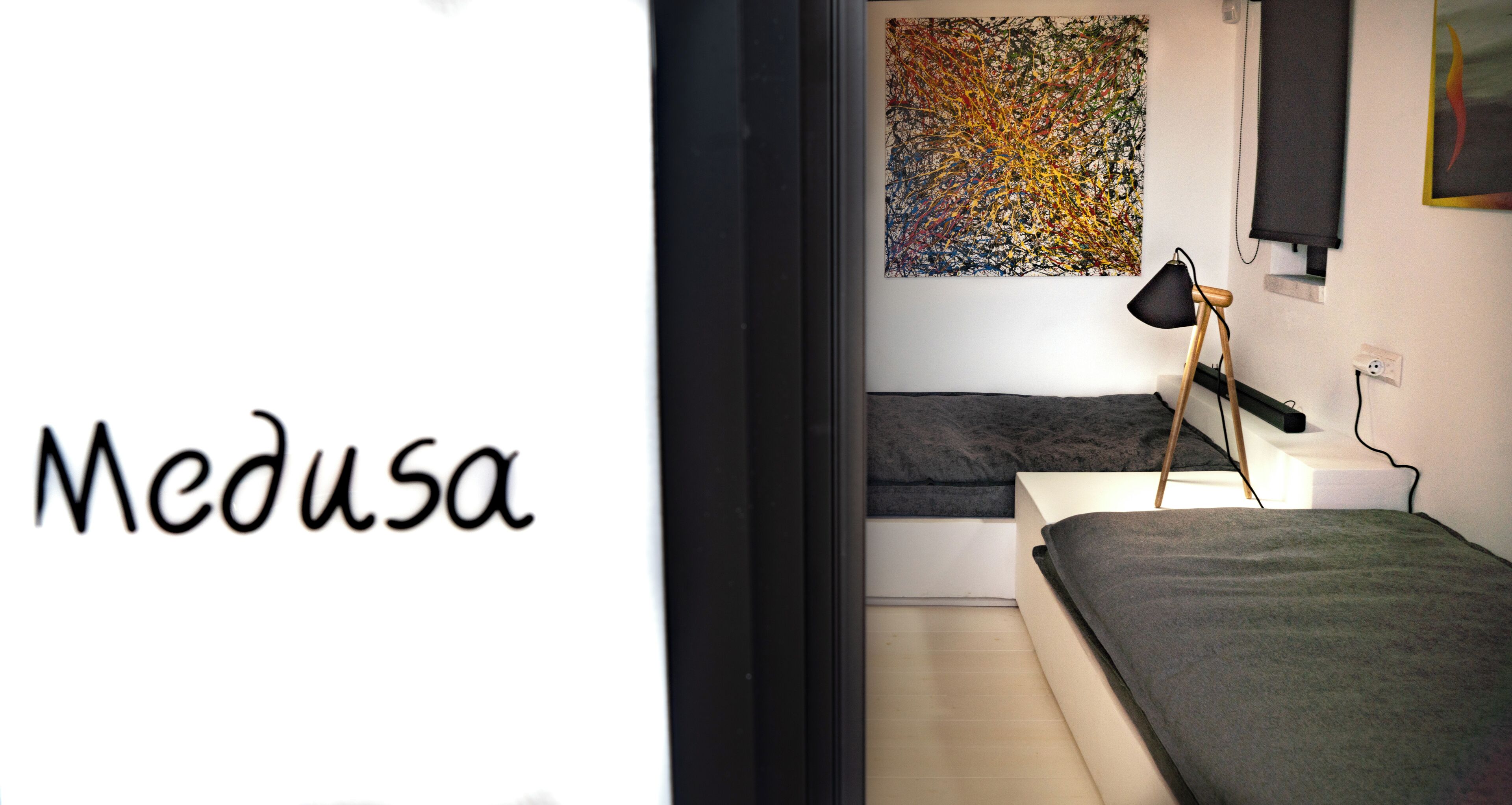A modern bedroom with a bed, a black lamp, and a colorful abstract painting on the wall.