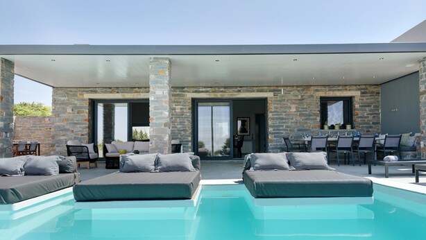 A modern outdoor pool area with stone walls, lounge chairs, and a covered seating area. - Apartment 'Drys Il' with Sea View, Wi-Fi and Air Conditioning (Ellinika)