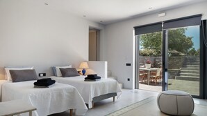 A modern hotel room with two beds, a small table, a chair, and a view of the outdoor area. - Apartment 'Drys Il' with Sea View, Wi-Fi and Air Conditioning (Ellinika)
