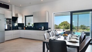 A modern kitchen with a dining area, large windows, and a view of a pool. - Apartment 'Drys Il' with Sea View, Wi-Fi and Air Conditioning (Ellinika)