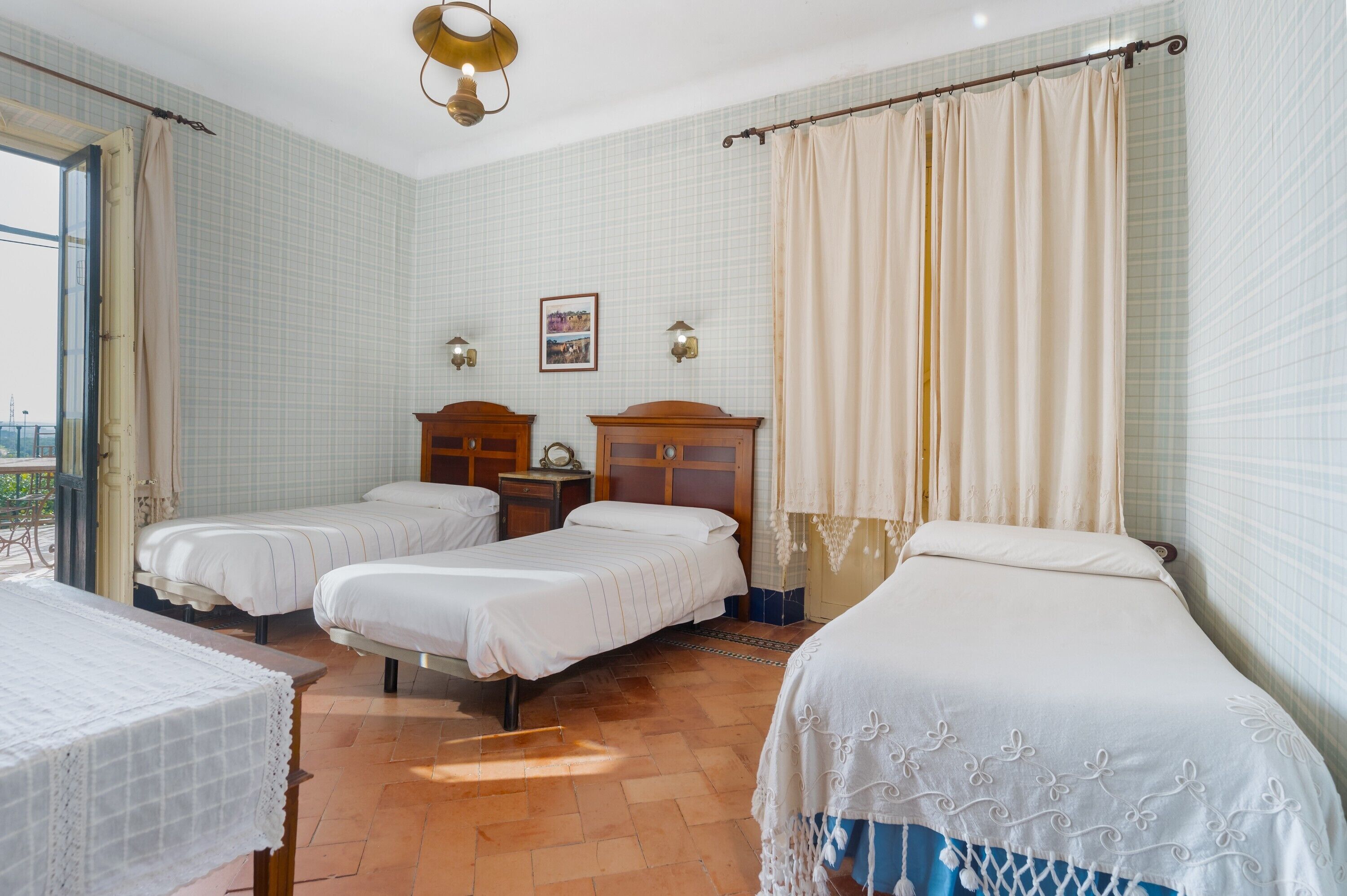 A hotel room with three beds, a wooden headboard, a small table, and a window with curtains.
