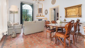 A dining area with a chandelier, patterned sofas, a fireplace, and a dining table with chairs.