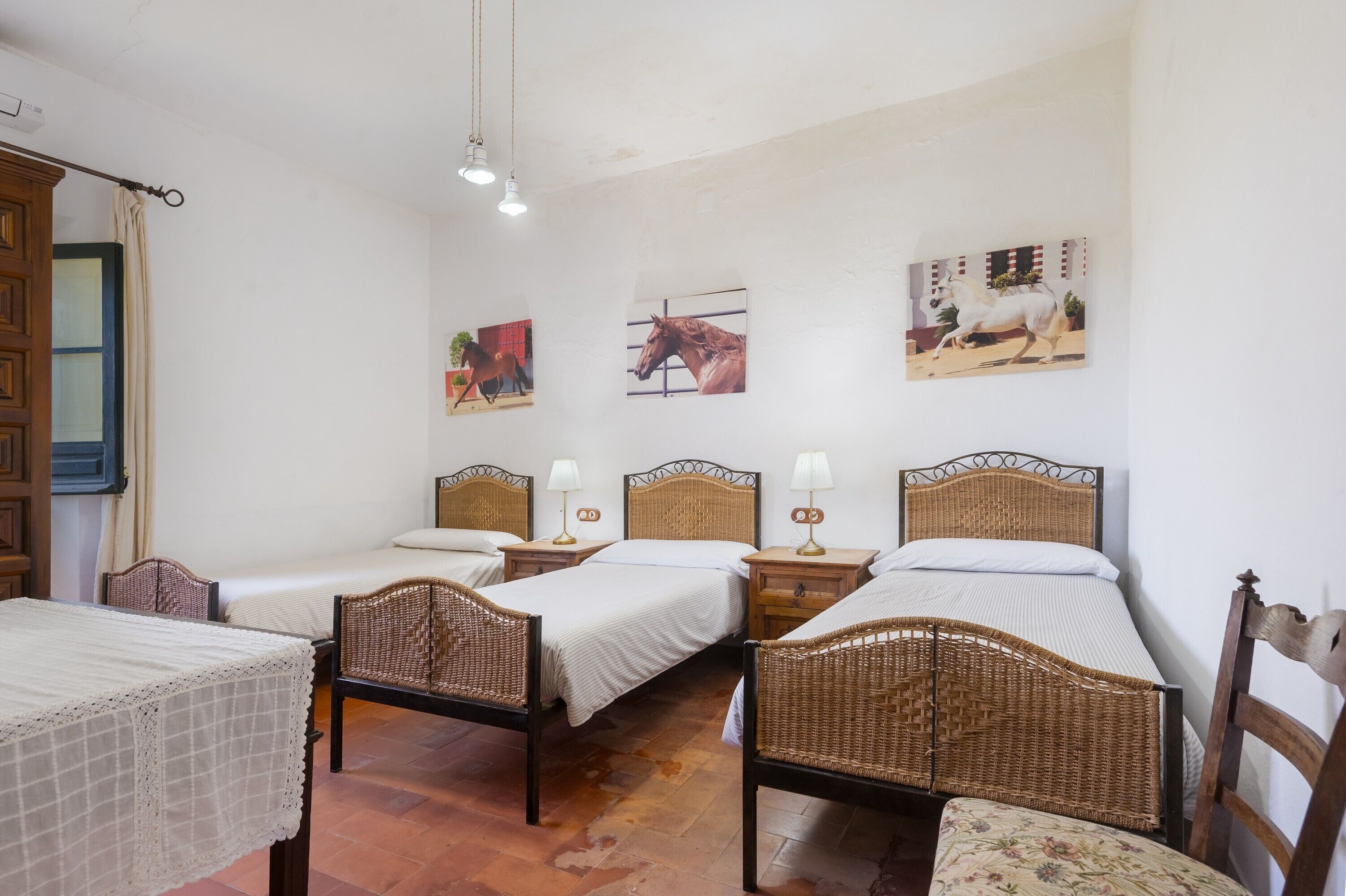 Ein Zimmer mit drei Einzelbetten, Rattan-Kopfteilen, Nachttischen mit Lampen und Wandbildern.