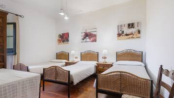 Ein Zimmer mit drei Einzelbetten, Rattan-Kopfteilen, Nachttischen mit Lampen und Wandbildern.