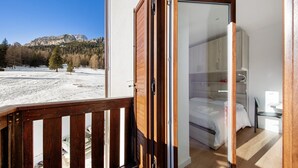 Une chambre avec un lit, un bureau et une vue sur un paysage enneigé, avec des arbres et des montagnes.