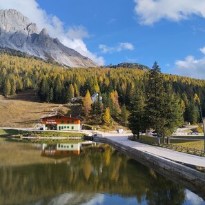 A lakeside view with a mountain in the background, a wooden building with a sign, and a reflection in the water.