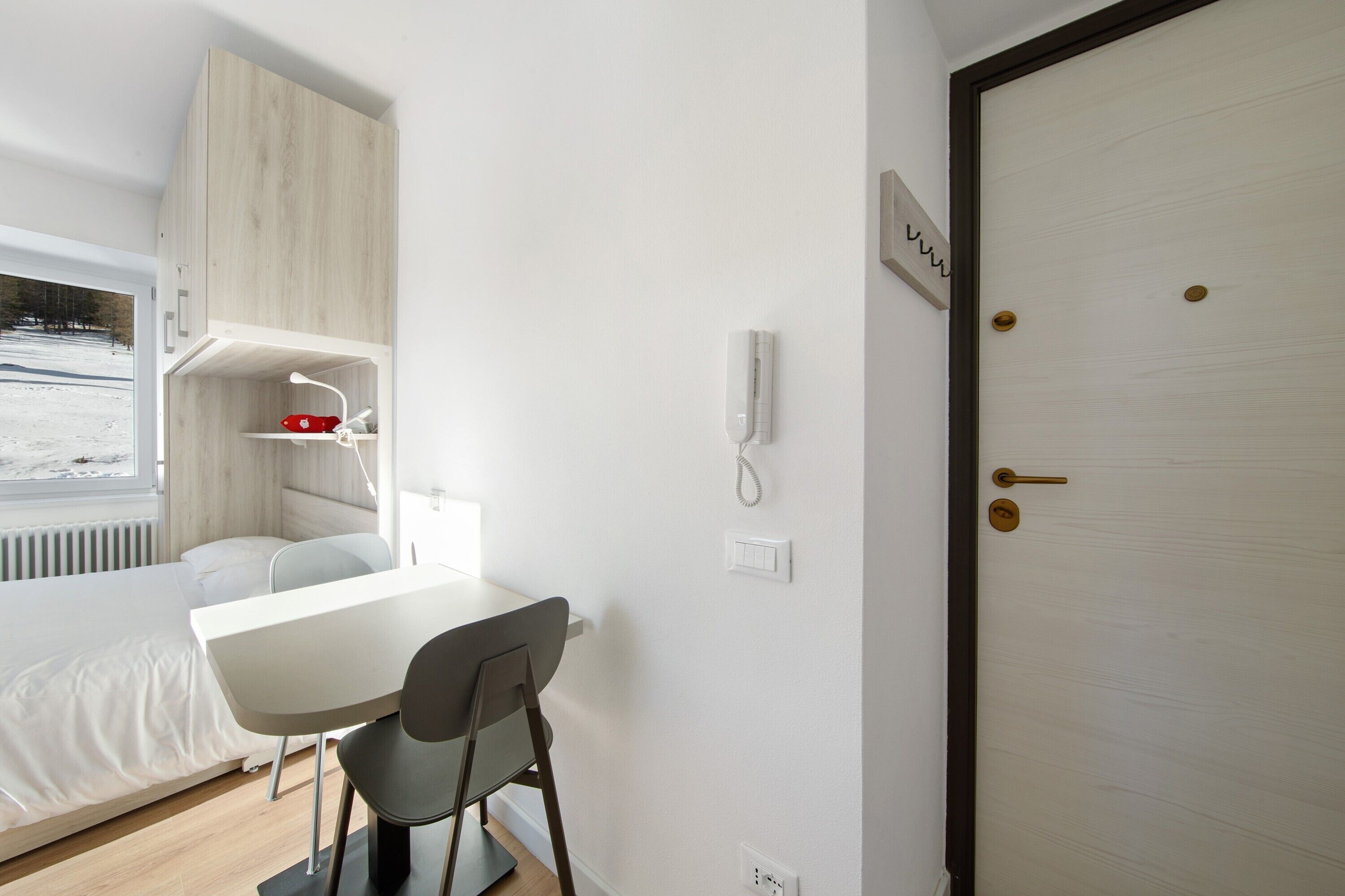 Een moderne kamer met een bed, een tafel en een stoel. Er is een raam met uitzicht op een besneeerd landschap.