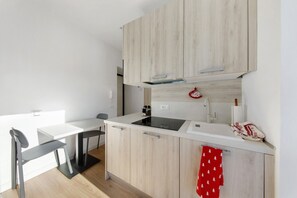 A modern kitchen with light wood cabinets, a white countertop, a black chair, and a red towel with a tree pattern.
