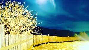 Scena notturna con una recinzione in legno, un vialetto lastricato e una luna luminosa nel cielo.