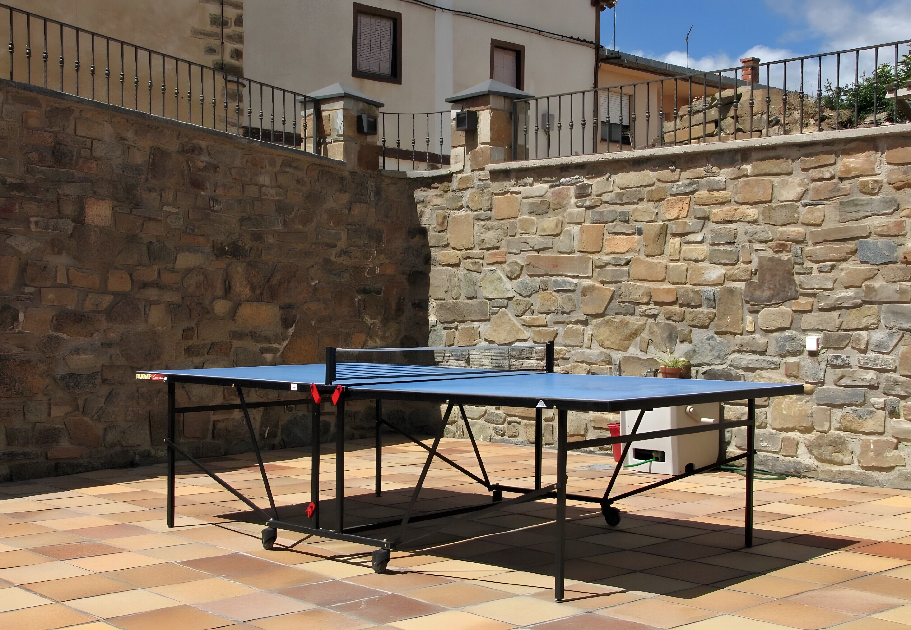 A ping pong table set up outdoors with stone walls and a metal railing in the background.
