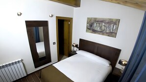 Una camera d'albergo con un letto, un comodino, un quadro appeso al muro, una porta e un termosifone.