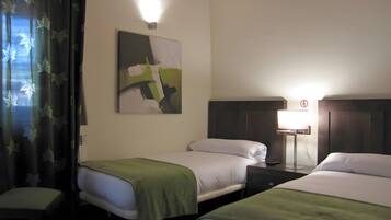 Quarto de hotel com duas camas, uma mesa de cabeceira, um abajur, um quadro na parede e uma janela com cortinas.