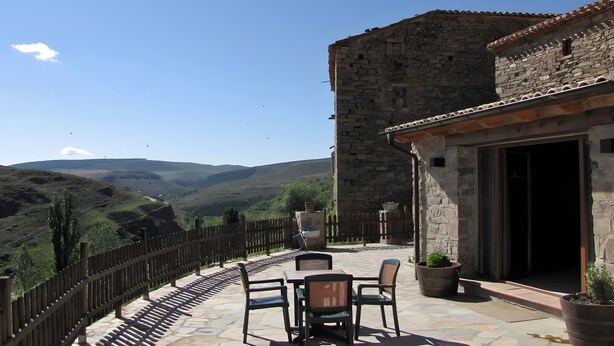 A stone building with a patio, outdoor seating, and a view of hills. - Spacious Country House 'El Ventorro' with Mountain Views (Bretún)