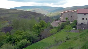 A rural landscape with a building featuring a red roof and white walls, surrounded by greenery and hills. - Cosy Countryside Retreat 'Las Rozas' with Mountain Views (Bretún)