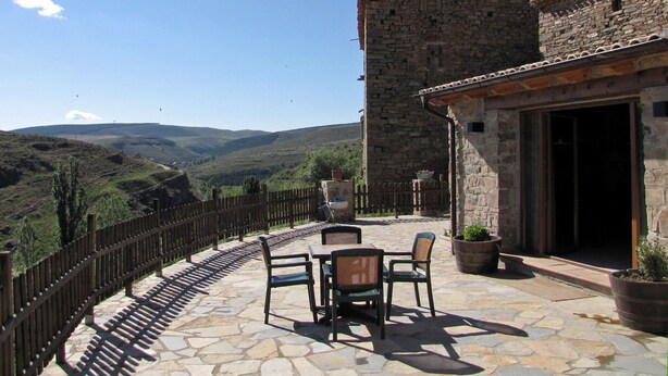 A stone patio with outdoor furniture, a stone building with a tiled roof, and a view of distant hills. - Cosy Countryside Retreat 'Las Rozas' with Mountain Views (Bretún)