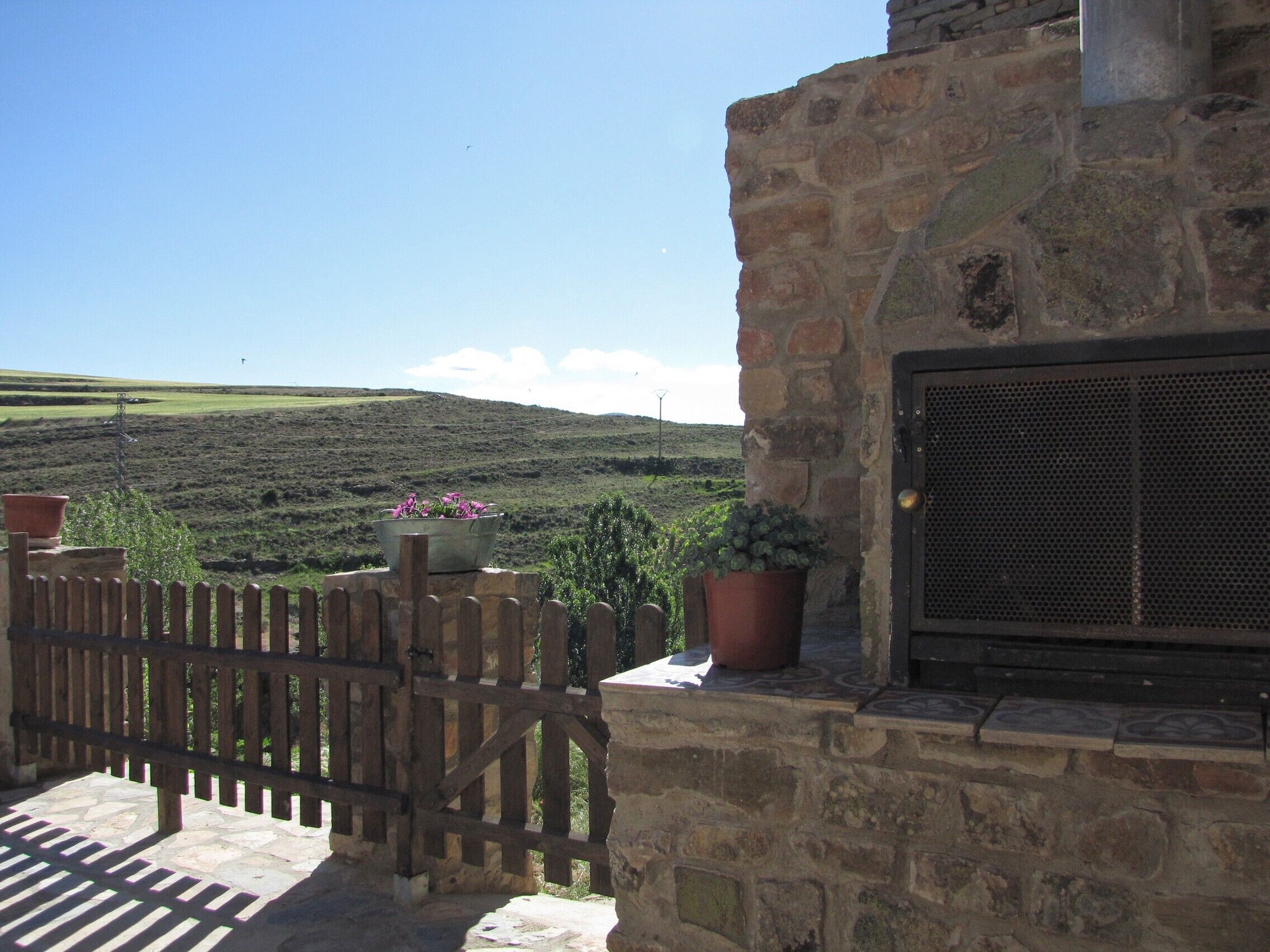A stone building with a wooden gate, potted plants, and a view of a hilly landscape.