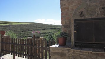 A stone building with a wooden gate, potted plants, and a view of a hilly landscape.