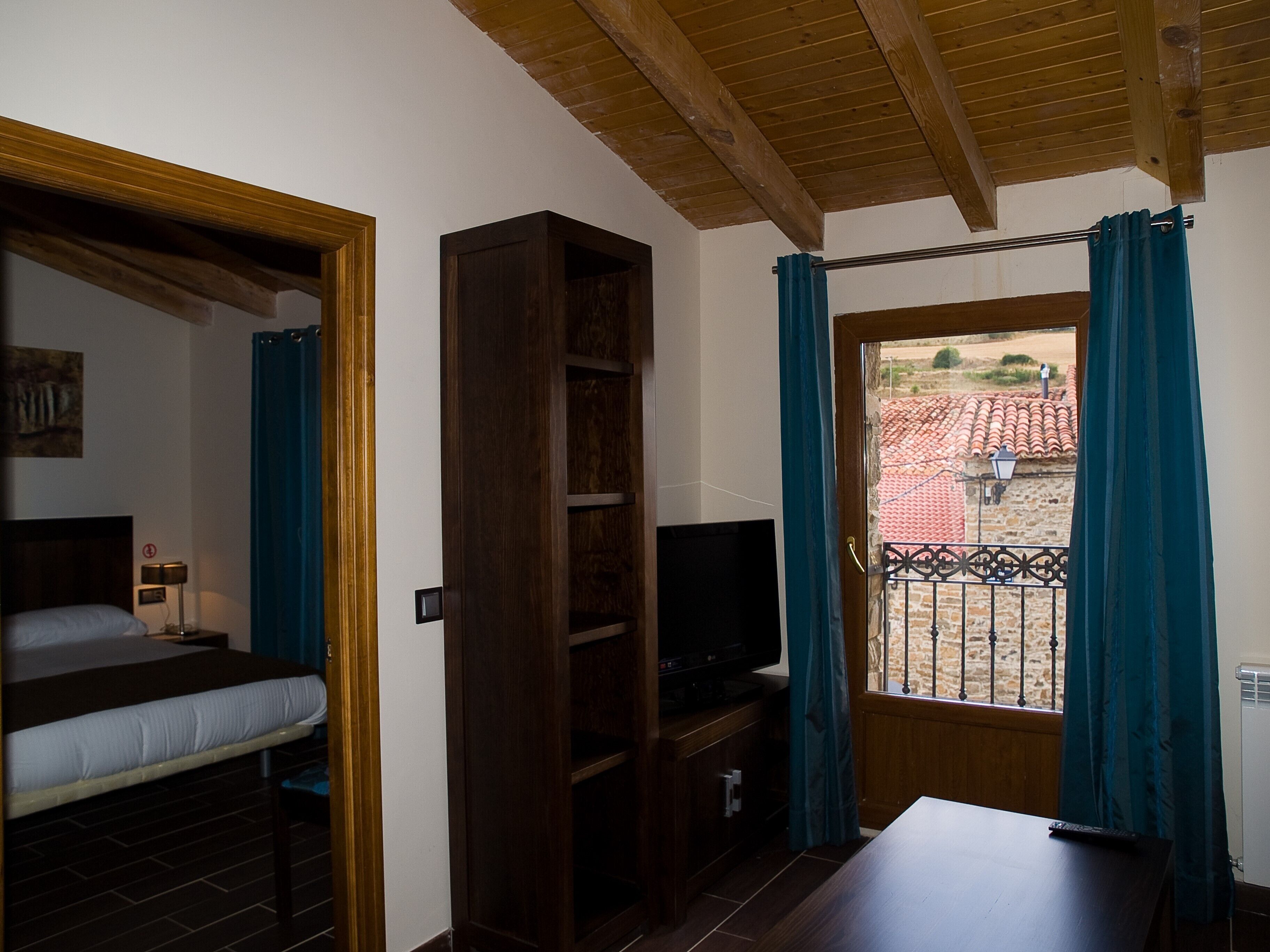 Une chambre à coucher avec un lit, une télévision, une armoire en bois et une fenêtre avec des rideaux.