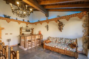A rustic interior with exposed brick walls, a wooden bar area, a floral sofa, and a chandelier.