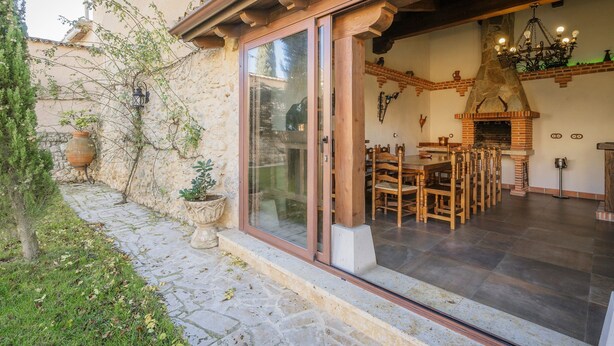 Un bâtiment en pierre avec une porte en verre, une cheminée et des meubles en bois à l’intérieur.