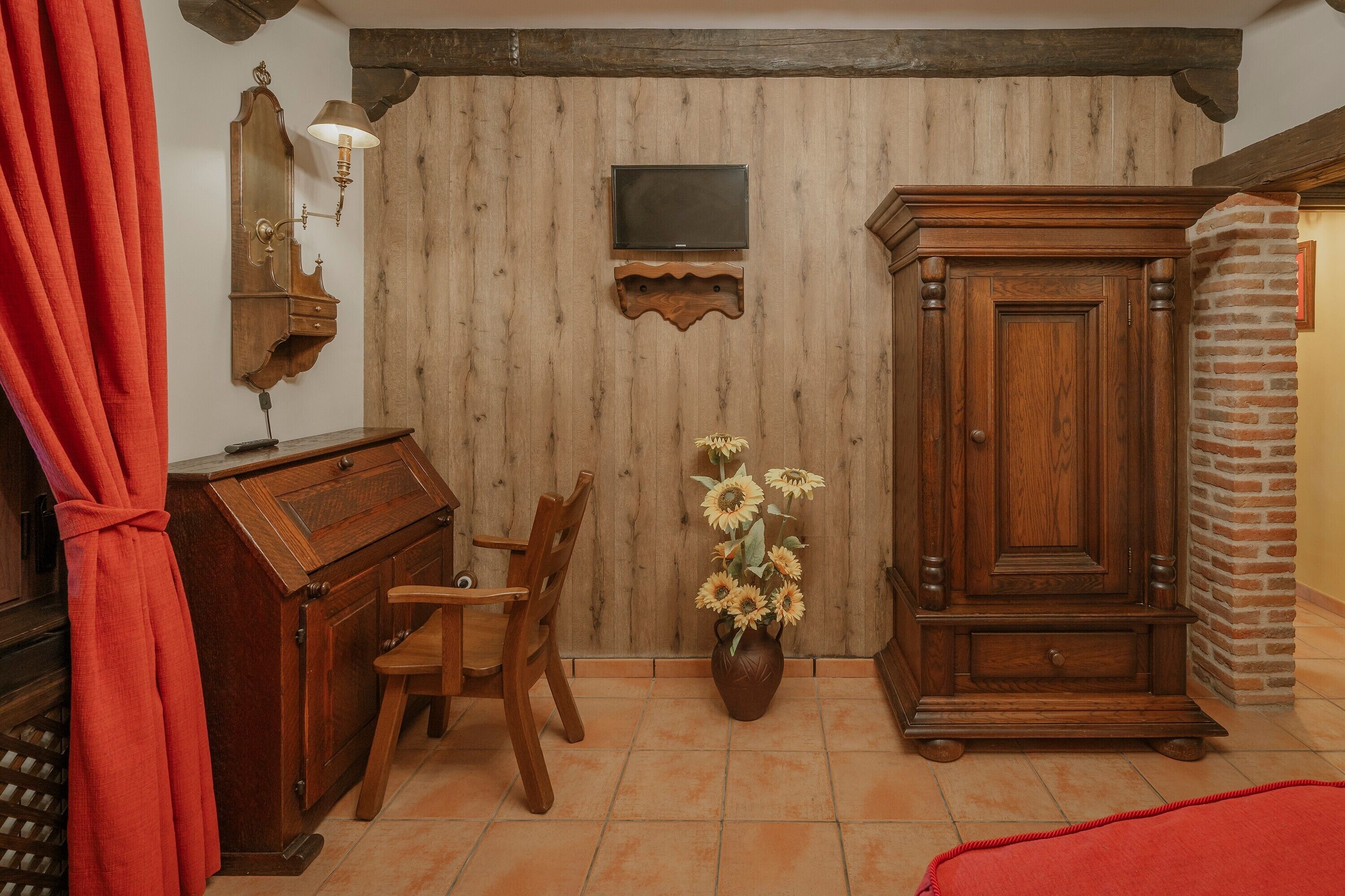 Une pièce comprenant un meuble en bois, un téléviseur fixé au mur, une chaise en bois et un vase avec des fleurs.