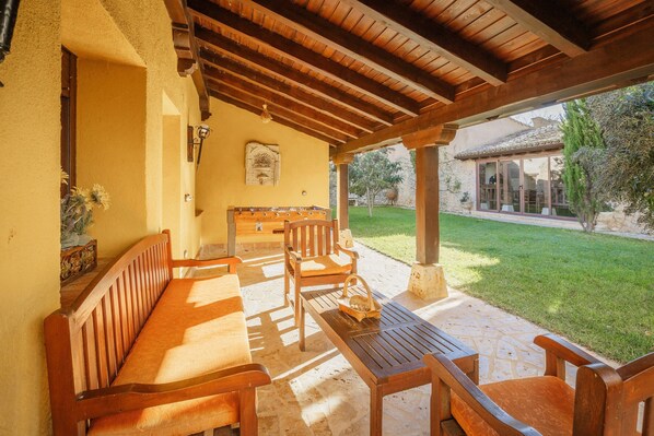 An outdoor patio with wooden furniture, a stone floor, and a view of a garden.