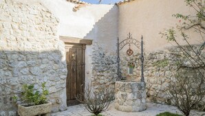 Une cour bordée de murs en pierre, avec une porte en bois et des plantes en pot.