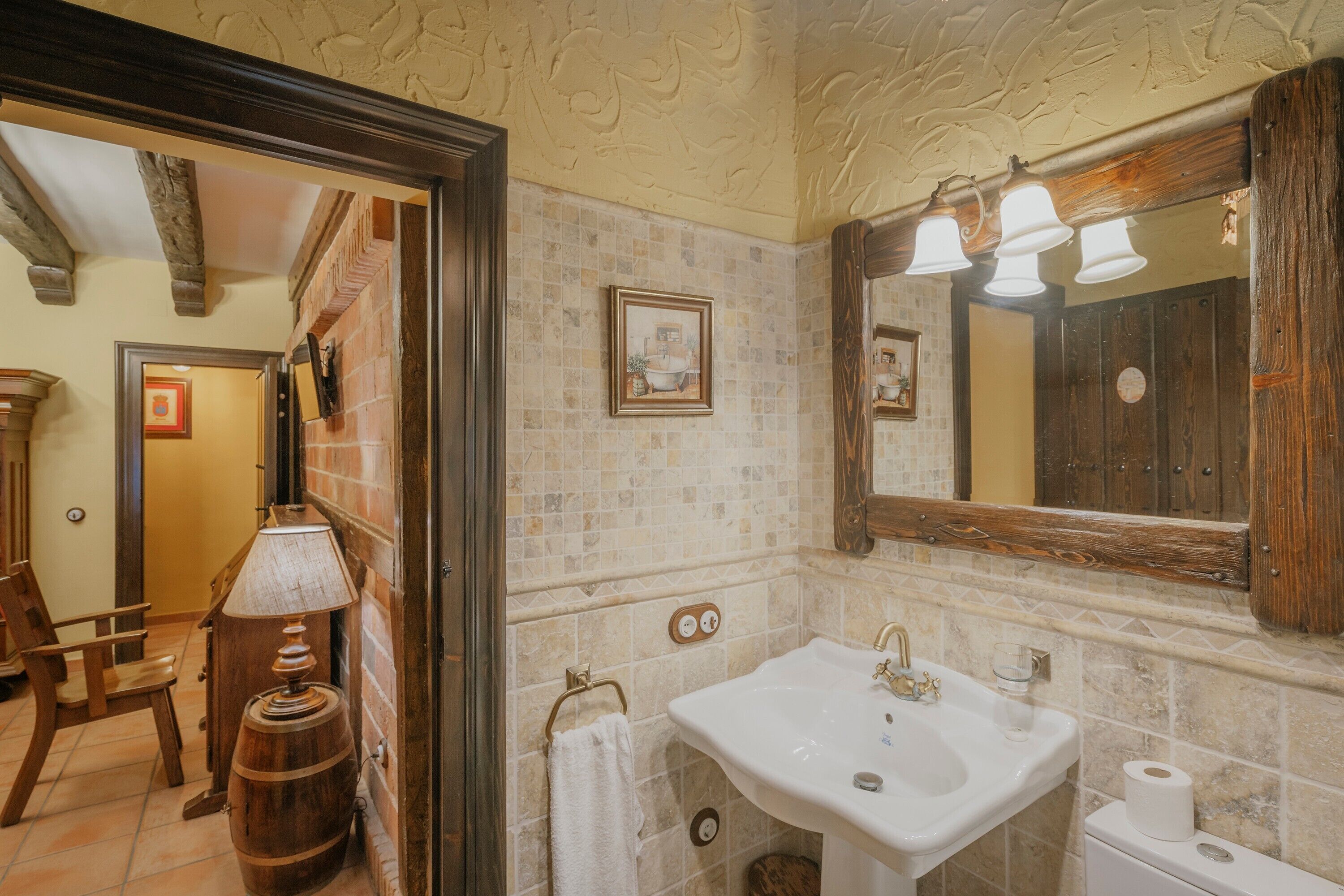 Un baño con lavamanos, espejo y un barril de madera.