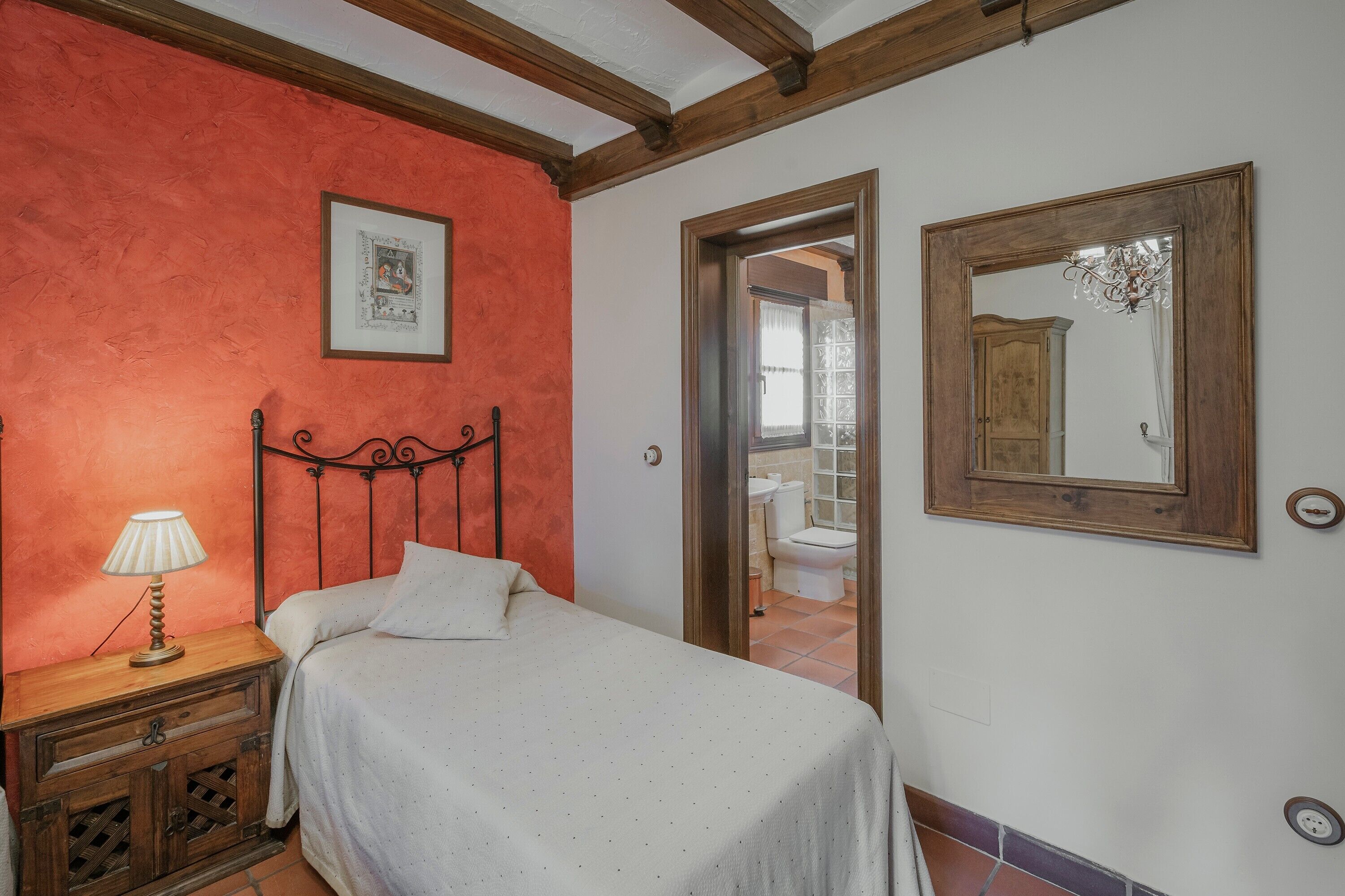 Een slaapkamer met een bed, een nachtkastje met lamp, een houten hoofdbord, een lijst met een foto aan de muur en een spiegel.